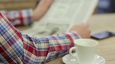 close up of male hands with newspaper, muffin and coffee cup on table