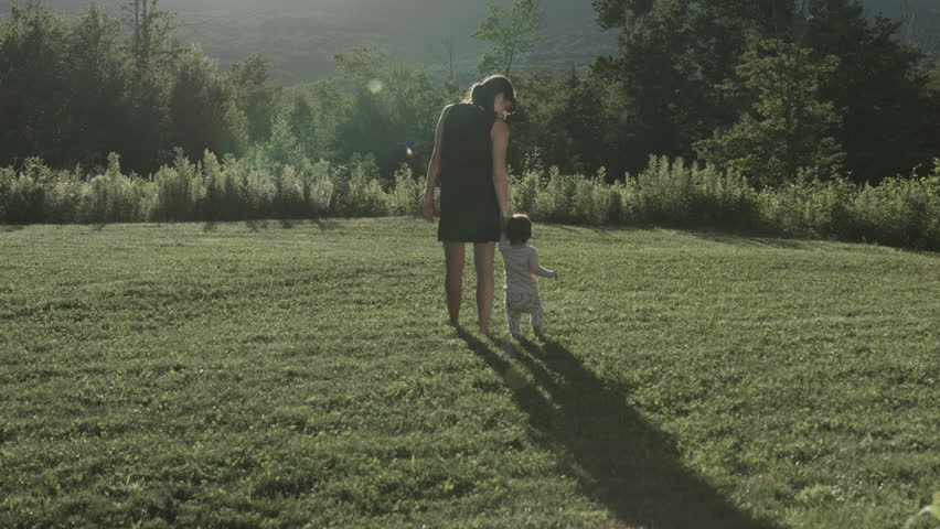 A mother and her child walking in a rural backyard on a sunny evening, shot in 4K in slow motion