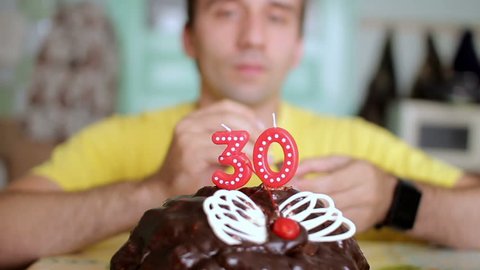 A man lights candles 30 years on a chocolate cake with butterfly wings. The man has a birthday today.
