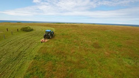 A farmer cutting the hay in his field on a beautiful ocean cape on the rocky coastline of Cape Breton Nova Scotia Canada