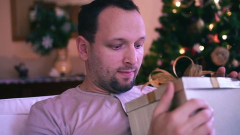 Amazed man looking at magical gift in the box, christmas tree in background Stock Video