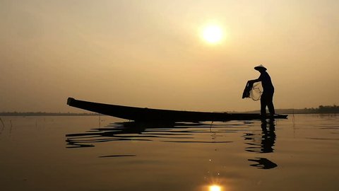 Silhouette of traditional fishermen throwing net fishing in the lake at sunrise time
