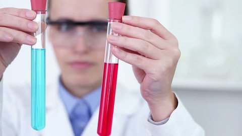 Female scientist comparing test tubes with red and blue fluid substance