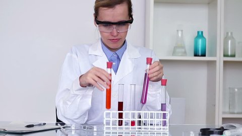 Female scientist comparing test tubes with chemicals and writing results