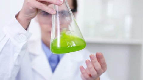 Female scientist mixing erlenmeyer flask with green chemicals