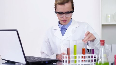 Female scientist examines test tubes and writing results on laptop
