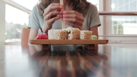 Young woman in cafe eating sushi with chopsticks