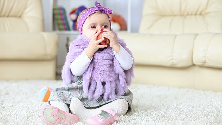 Girl child is sitting on the floor eating an apple