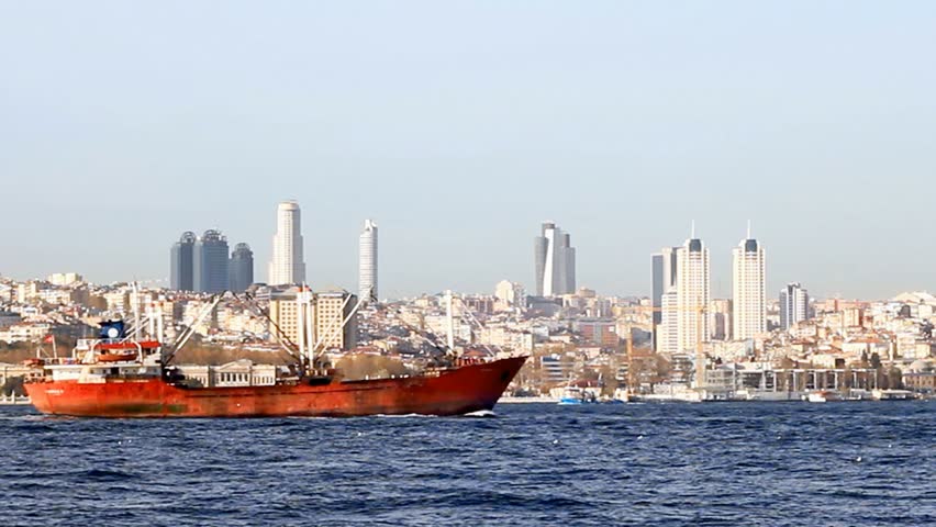 Red cargo ship sails in front of the city