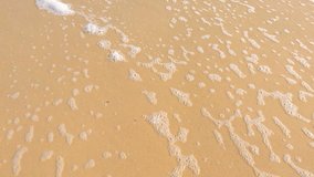 Close up of ripples and rolling waves on a sandy beach, handheld. 
