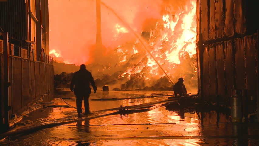 Firemen silhouetted at a large industrial fire
