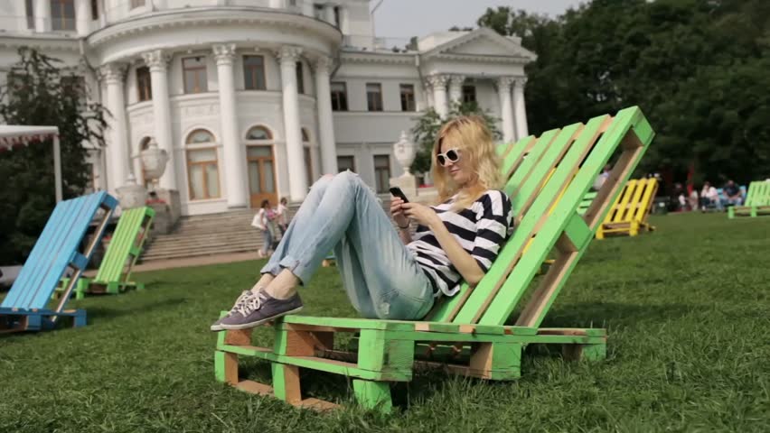 Beautiful Girl With Phone Resting on a Wooden Lounger on the Nature