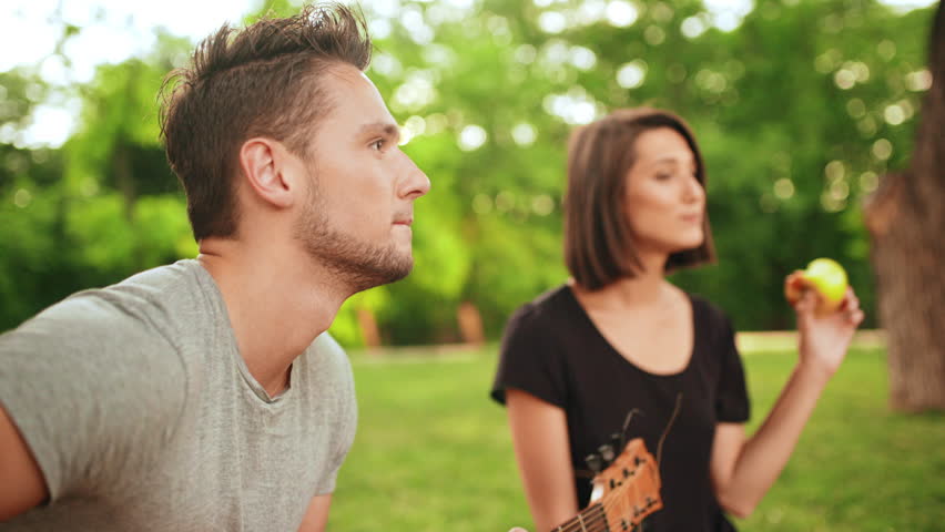 Young beautiful couple smiling, resting in park. Man playing guitar.