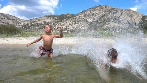 Slow motion: Young boys running and swimming in the lake on mountains background
