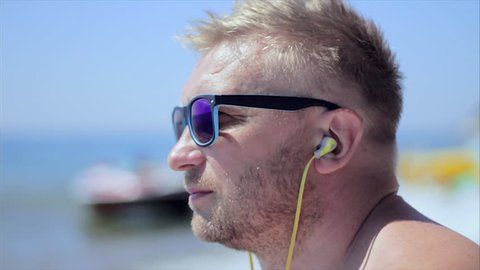 Young bearded man with headphones and sunglasses listening music on sea background