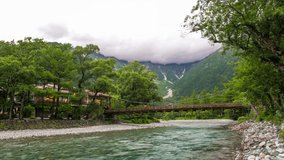 Zoom out evening time-lapse of transitioning night darkness, clouds above mountains, Kappabashi bridge, flowing river and village at pristine nature of summer destination Kamikochi in Japanese Alps