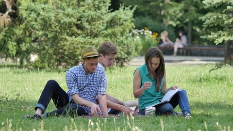 Young People Are Sitting on a Lawn and Reading, Studying Outdoors. Students, Girls and Boys Are Leafing Through the Books, Pointing to the Page, Preparing to Exams, Doing the Hometask, Smiling, Have