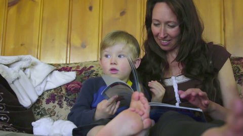 Mother and son read a book on the living room couch when the child decides to get up and leaves