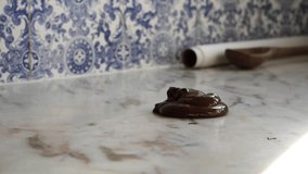 Homemade culinary artisan tempering smooth dark chocolate confectionery on marble counter with blue and white tiles in background.