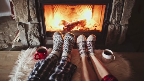 Couple Feet in Woollen Socks by the Cozy Fireplace, 4K. Man and Woman relax by warm fire and warming up their feet. Close up. Winter and Christmas holidays concept.  Video stock