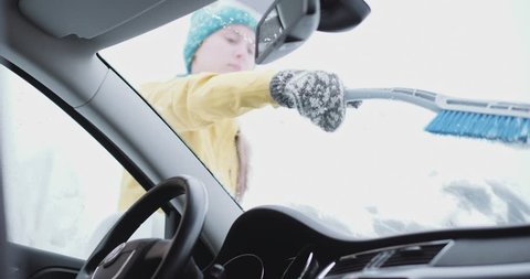Young woman cleaning Snow and Ice off her Car wind shield window. Slow Motion, 4K DCi. Unrecognizable Woman brushes off the snow from parked car. Winter snow storm, safe driving, weather challenge. 스톡 비디오