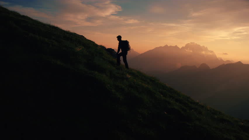 Aerial - Epic shot of a man hiking on the edge of the mountain as a silhouette in beautiful sunset (edited version) Royalty-Free Stock Footage #18955577