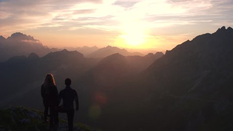 Aerial - Flyover hiking couple watching beautiful sunset in the mountains