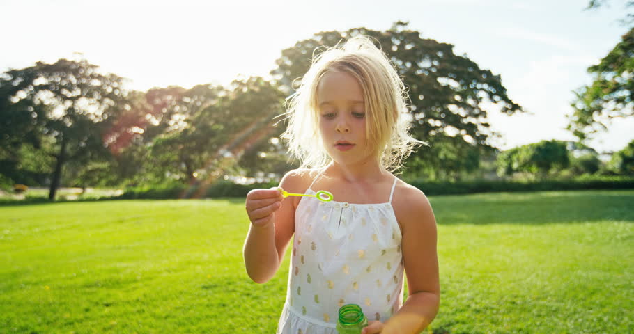 Adorable cute young girl blowing bubbles playing outside