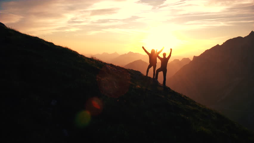 Aerial, edited - Rising above hiking couple celebrating successful climb on the mountain with raising arms at beautiful sunset Royalty-Free Stock Footage #18955649