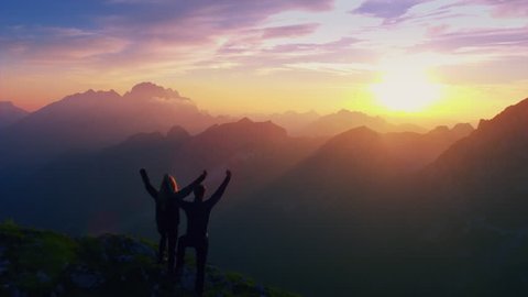 Aerial, edited - Silhouette of a couple with raised arms celebrating successful climb on the mountain in beautiful sunset