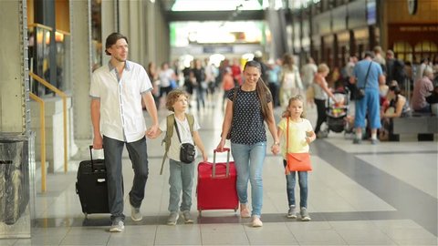 Happy family with little girl and boy going on railway station, mother father and the kids walk through the airport with suitcases, travel