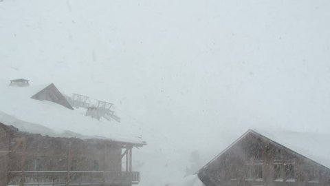 Snow blowing by a chalet in the French Alps. Cable car moving in the background.
