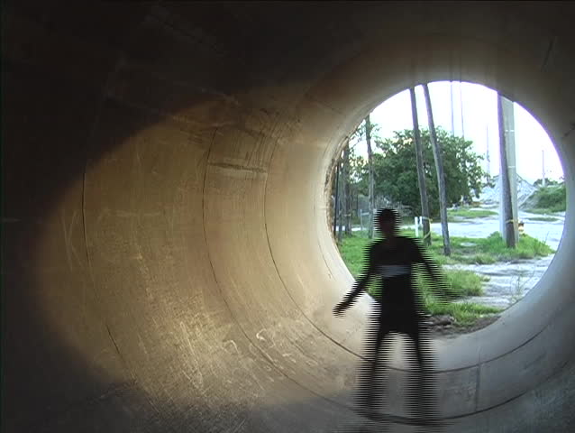 A skateboarder rides inside of a drainage tunnel.