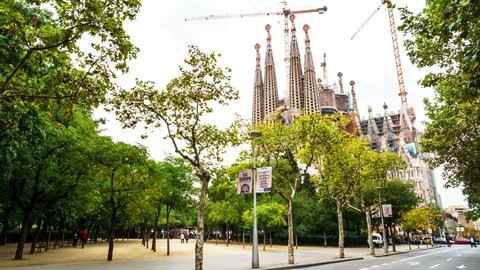 BARCELONA, SPAIN - OCTOBER 24, 2015: Famous Sagrada Familia Cathedral behind the trees. Designed by Antoni Gaudi in Gothic Style is under construction. UNESCO World Heritage Site. Cloudy grey sky