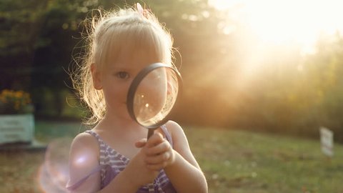 Girl looking through a magnifier at sunset