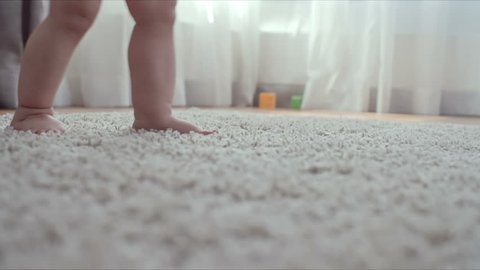 Closeup of tiny barefoot legs of baby walking on the soft rug without any help