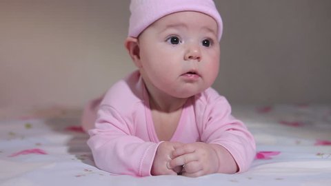 A cute funny little baby lying on her stomach and wearing a pink hat. Vídeo Stock