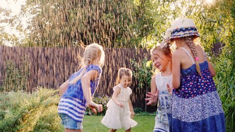 Carefree fun children play in the garden. Laughing, running under the jets of water or rain