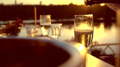 Pouring Champagne. People toasting and drinking champagne on the restaurant terrace over sunset. Celebrating. Glasses with Sparkling Champagne over nature Background. Resort. Slow motion full hd 1080p