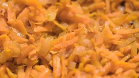 Chopped onions and carrots fried in vegetable oil in the pan. Close-up on top of a kitchen tile. 