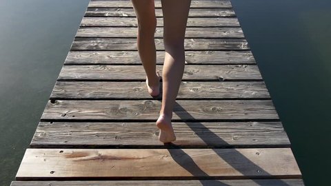 Woman walks on wooden pier in a summer day after jogging and dives into the water, slow motion