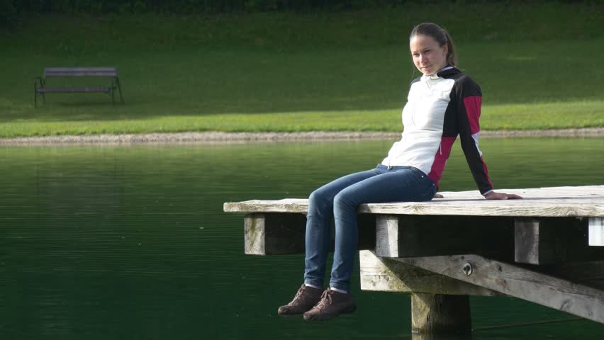 Relaxed woman sits on the pier, smiles and enjoys a sunny day