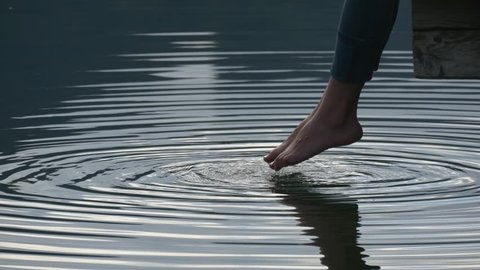 Circles on the blue clear water with reflecting sky from swinging bare feet of woman sitting on pier