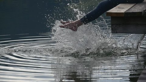 Woman feet dipped into the lake splash water into big wave and lots of shining drops, slow motion