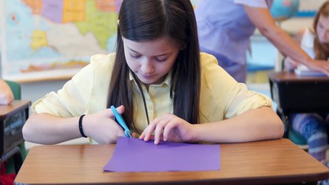 A young girl does arts and crafts at school by cutting colored paper.