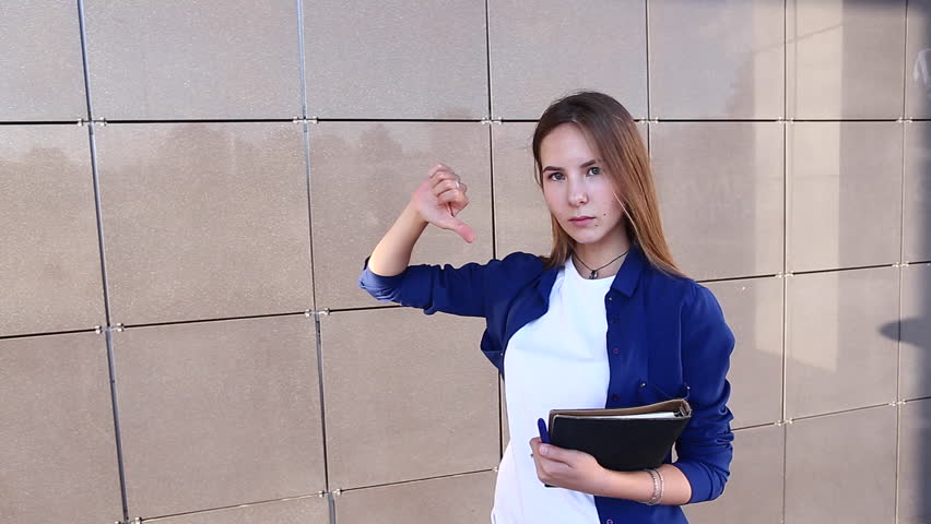 Woman Girl Lady Portrait Looking Camera Walking and Shows Thumbs up Down Like Dislike. Young Beautiful Student Business Female With Long Hair on the Background Building.