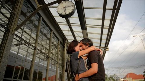 Happy couple embracing on railway station platform. Farewell at the train station, young girl and guy talking on platform