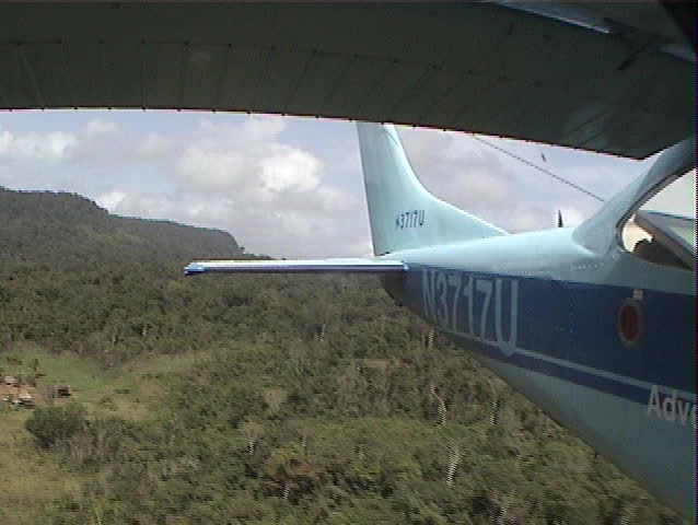 Rear facing aerial shot from a plane landing on a grass airstrip in the jungle