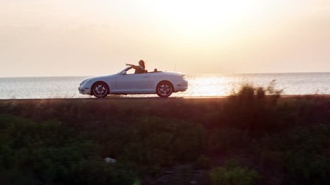 Man And Woman Driving Convertible Car By The Beach At Sunset Vacation Girl Happy Wind Blowing Hair Summer Joy Holiday Happiness Romantic Couple Honeymoon Concept Drone Aerial