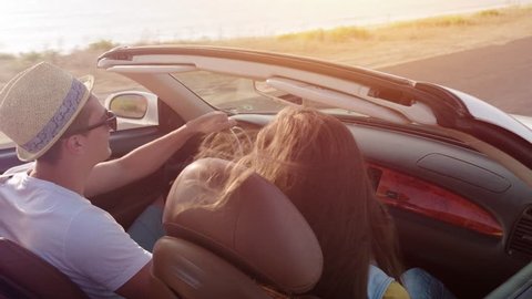 Young Man And Woman Driving A Convertible On Sea Road Beach Front Enjoying Summer Happiness Vacation Adventure Travel Luxury Car Exotic Destination Concept
